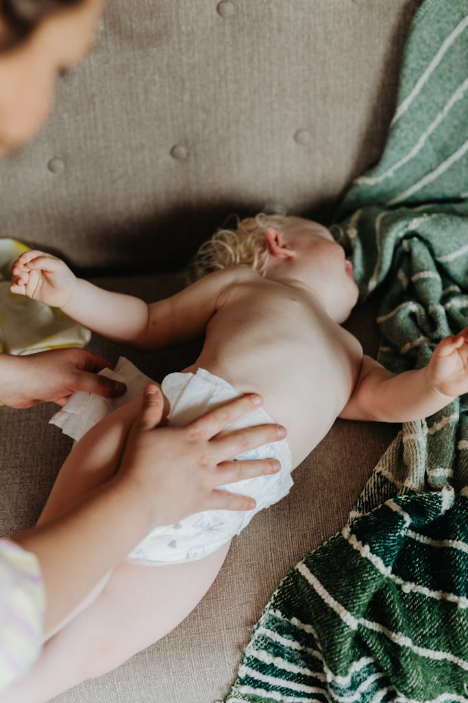 A nurturing moment of a mother changing her baby's diaper on a cozy couch indoors.